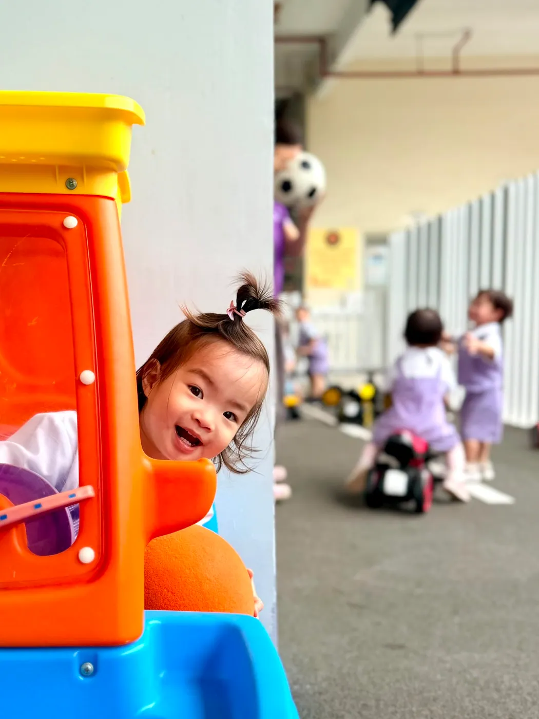 A toddler smiling from a ride-on car at the outdoor playground